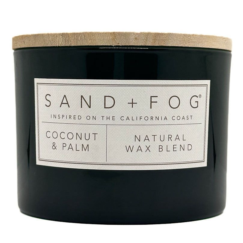 Coconut & Palm Candle black candle with a white label and wooden lid labeled 'Sand + Fog' on a white background