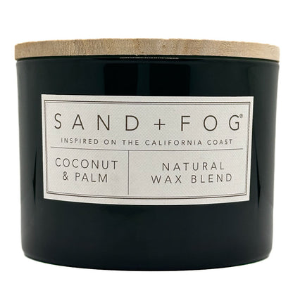 Coconut & Palm Candle black candle with a white label and wooden lid labeled 'Sand + Fog' on a white background
