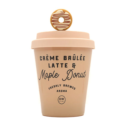 A light peach-colored ceramic coffee cup designed like a takeaway latte container, featuring a lid with a donut-shaped handle and printed text reading 'CRÈME BRÚLÉE LATTE & Maple Donut' on a white background.