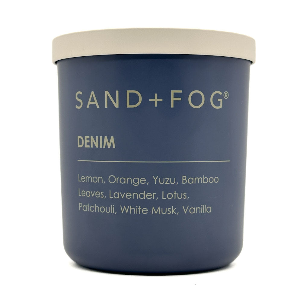 Blue candle jar with 'Sand + Fog' branding and 'Denim' scent description on a white background