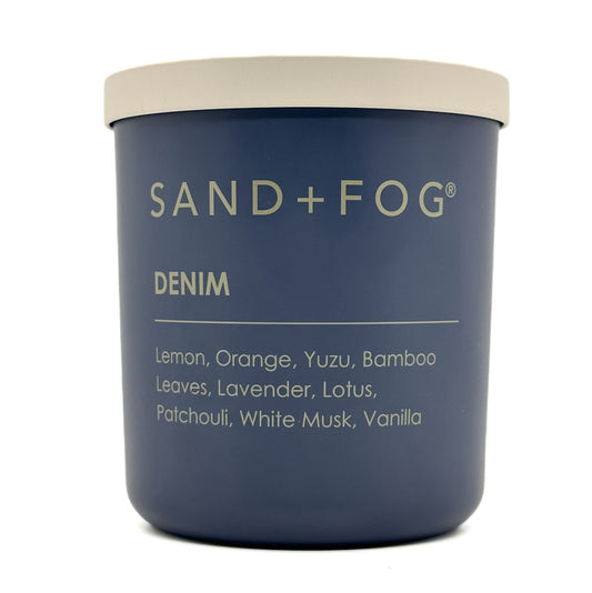 Blue candle jar with 'Sand + Fog' branding and 'Denim' scent description on a white background