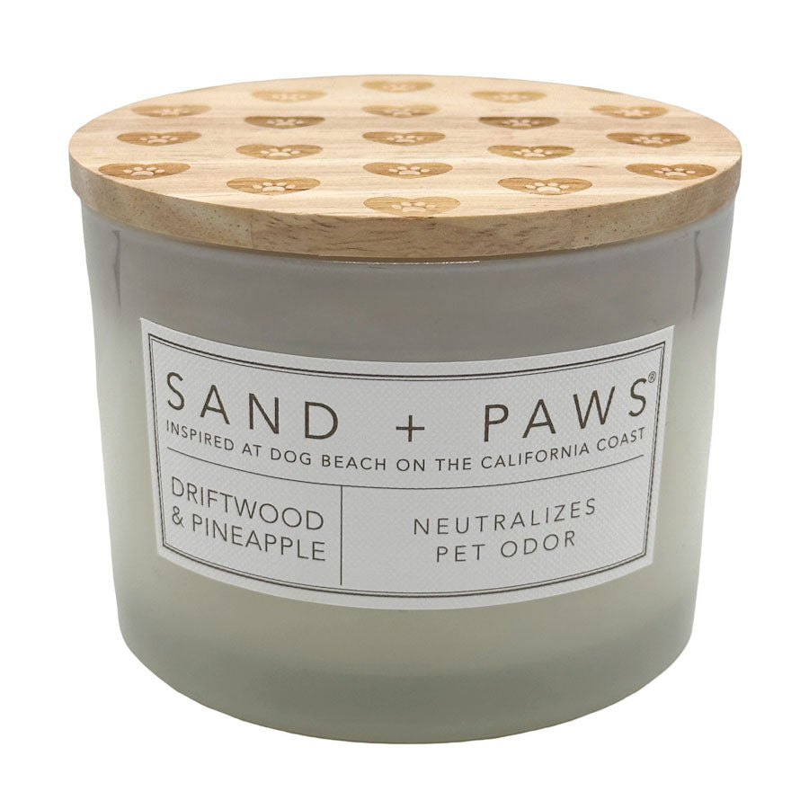 Driftwood & Pineapple candle with wooden lid labeled 'Sand + Paws' on a white background