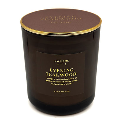 A dark brown glass jar candle with a matching brown lid and gold trim, featuring a front label that reads 'DW HOME EVENING TEAKWOOD'.