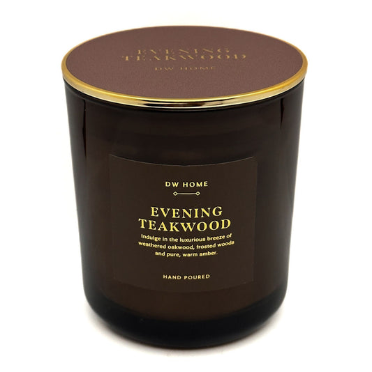 A dark brown glass jar candle with a matching brown lid and gold trim, featuring a front label that reads 'DW HOME EVENING TEAKWOOD'.