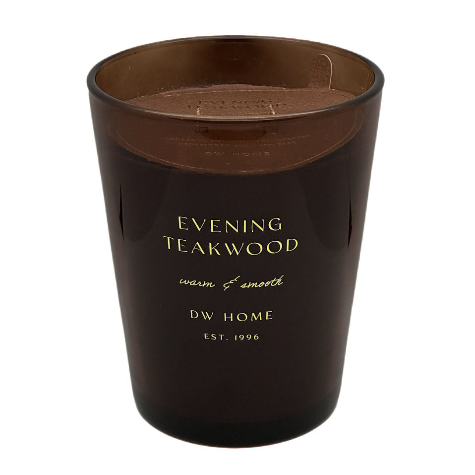 An amber glass jar candle with gold lettering that reads 'EVENING TEAKWOOD' and 'DW HOME EST. 1998' on a white background.