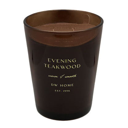 An amber glass jar candle with gold lettering that reads 'EVENING TEAKWOOD' and 'DW HOME EST. 1998' on a white background.