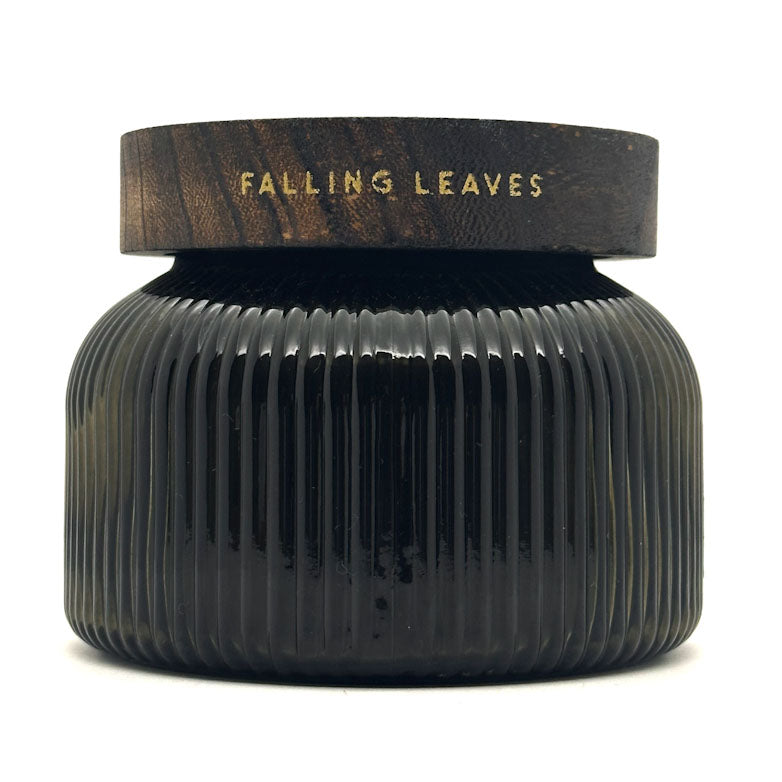 A dark ribbed glass jar with a matching dark wood lid, featuring the words 'FALLING LEAVES' in gold lettering, set against a plain white background.