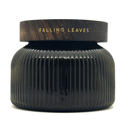 A dark ribbed glass jar with a matching dark wood lid, featuring the words 'FALLING LEAVES' in gold lettering, set against a plain white background.