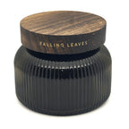 A dark ribbed glass jar candle with a round wooden lid printed with the scent name 'FALLING LEAVES' in gold lettering, set against a plain white background.