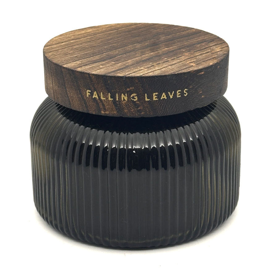A dark ribbed glass jar candle with a round wooden lid printed with the scent name 'FALLING LEAVES' in gold lettering, set against a plain white background.