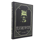 A hardcover Notebook of Frankenstein by Mary Shelley, featuring a black cover with a pale green illustration of the creature's face and ornate vintage-style borders, shown standing upright on a white background.