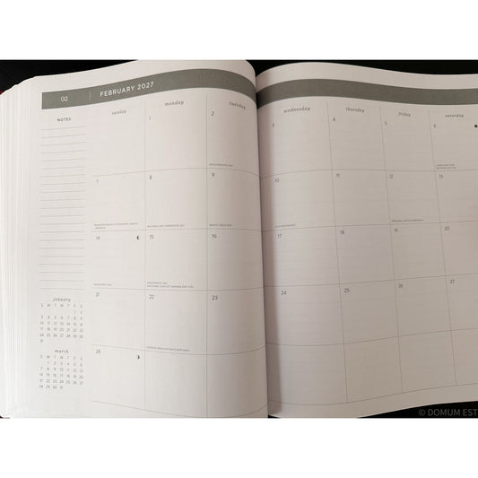 An open planner or calendar showing the February 2027 weekly layout with columns for Monday through Sunday and a small monthly calendar at the lower left, photographed against a dark background.