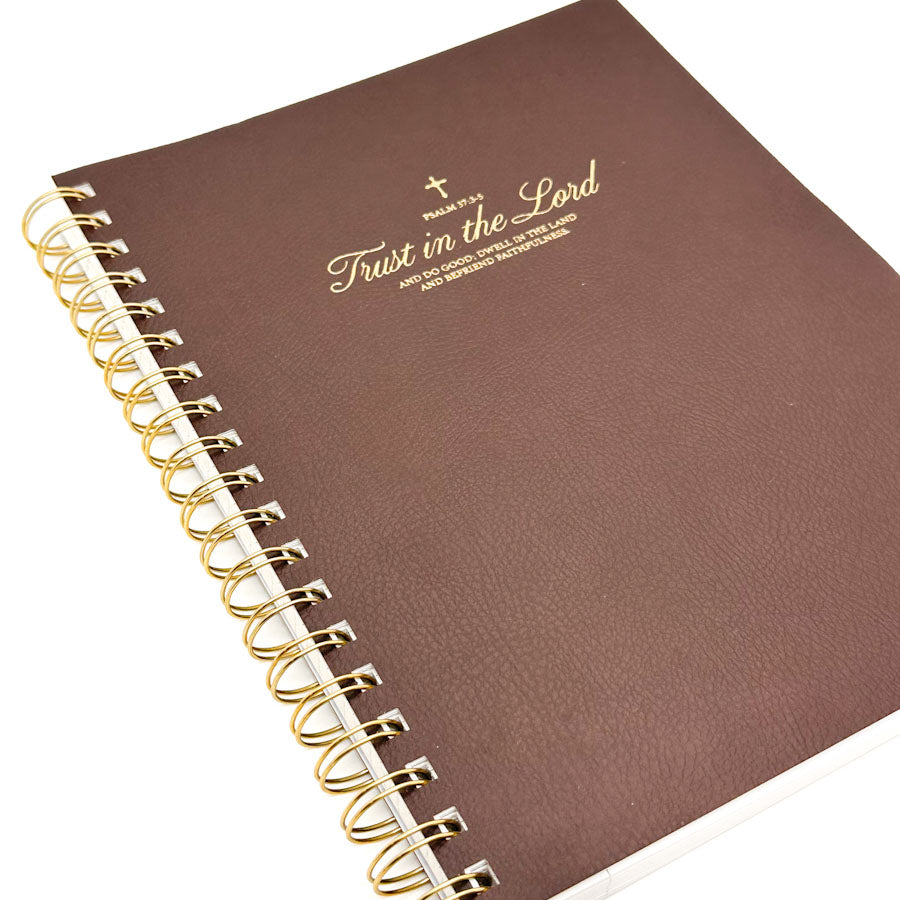 A brown faux-leather spiral notebook with gold foil text reading 'Trust in the Lord' and a gold wire binding, shown on a white background.