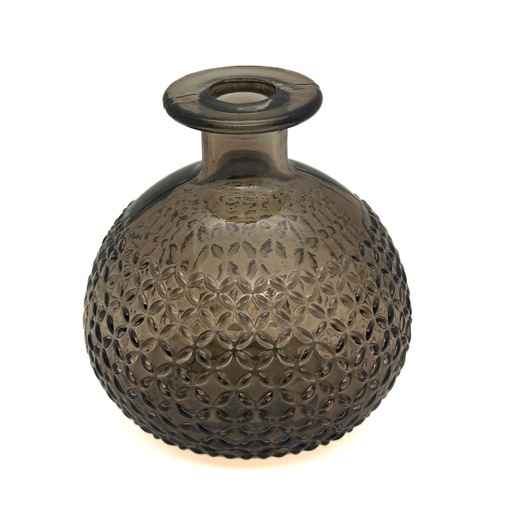 A round, bulb-shaped glass vase with a short flared neck and a textured, embossed floral pattern, made of translucent smoky brown glass, shown on a white background with a warm glow at the base.