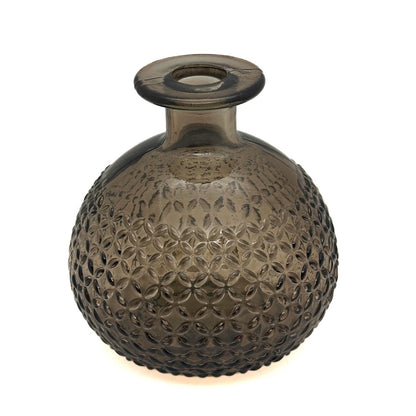 A round, bulb-shaped glass vase with a short flared neck and a textured, embossed floral pattern, made of translucent smoky brown glass, shown on a white background with a warm glow at the base.