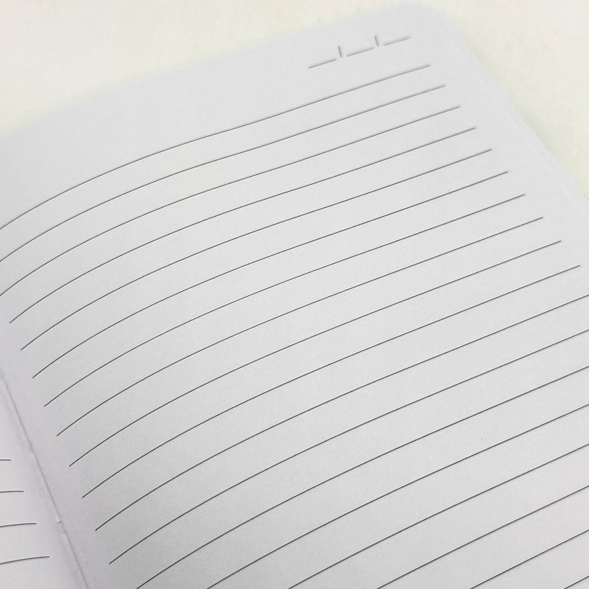 A close-up of a lined notebook page with horizontal black lines on white paper, photographed on a light neutral background.