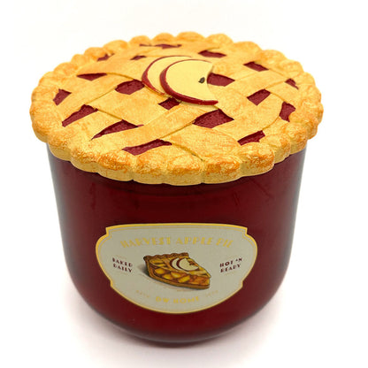 A novelty candle shaped like a pie jar with a golden-brown lattice crust lid and a red body, labeled 'Harvest Apple Pie' by DW Home, on a white background.