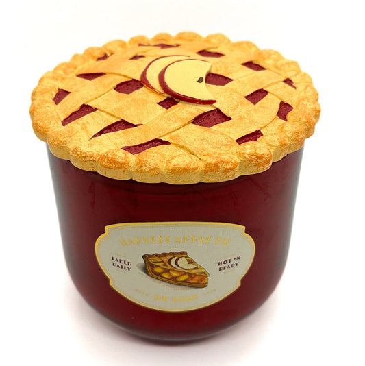 A novelty candle shaped like a pie jar with a golden-brown lattice crust lid and a red body, labeled 'Harvest Apple Pie' by DW Home, on a white background.