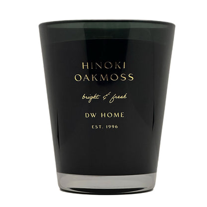 A black glass candle jar with gold lettering that reads 'HINOKI OAKMOSS', 'bright & fresh', and 'DW HOME EST. 1996' on a plain white background.