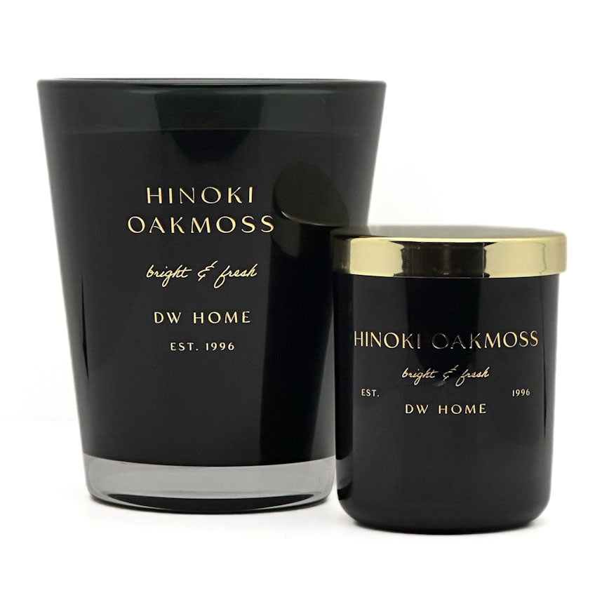 Two black Hinoki Oakmoss scented candles by DW Home, one large glass jar and one smaller jar with a gold lid, on a white background.