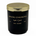 A black glass jar candle with a metallic gold lid, featuring gold lettering that reads 'HINOKI OAKMOSS', 'bright & fresh', 'EST. 1996', and 'DW HOME' on a clean white background.