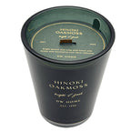 A black glass jar candle with a dark green wax surface and a matching dark green lid. The lid features gold text reading 'HINOKI OAKMOSS bright & fresh' and 'DW HOME'.