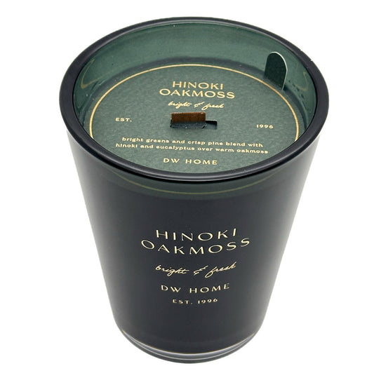 A black glass jar candle with a dark green wax surface and a matching dark green lid. The lid features gold text reading 'HINOKI OAKMOSS bright & fresh' and 'DW HOME'.
