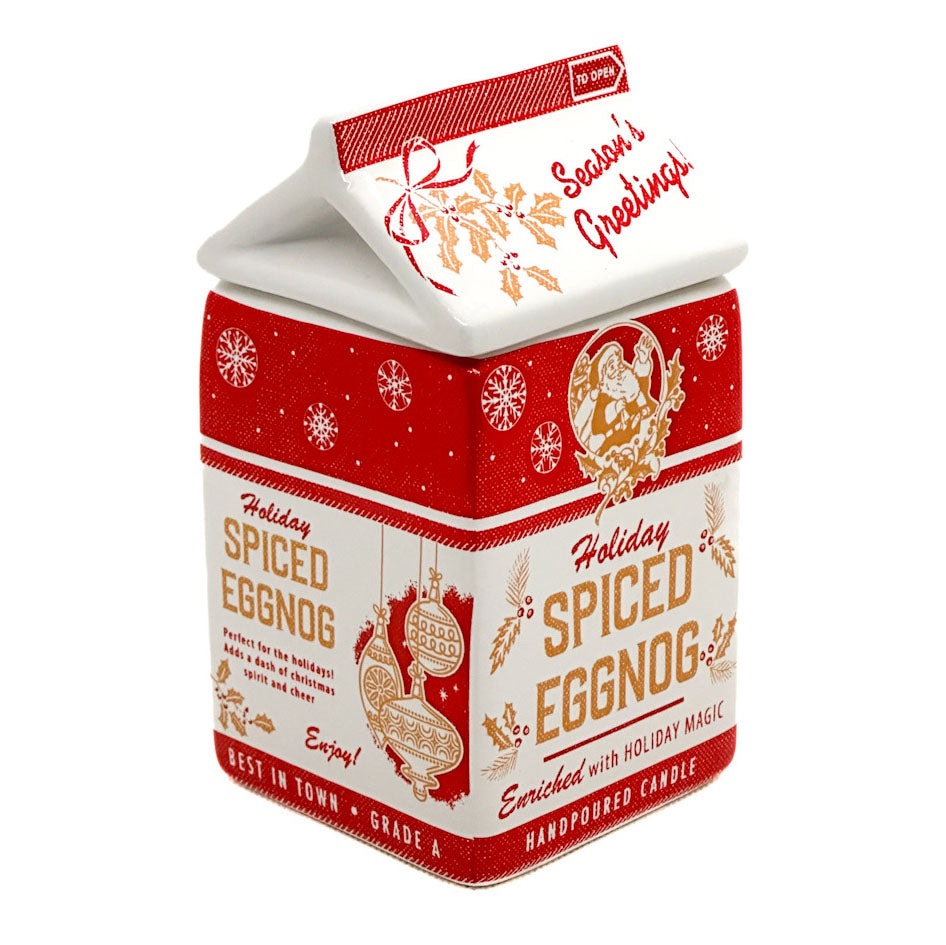 A house-shaped handpoured candle in a red and white carton design with holiday illustrations and the text 'Holiday Spiced Eggnog' and 'Season's Greetings'.