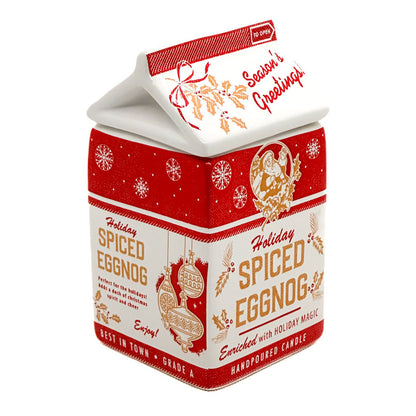 A house-shaped handpoured candle in a red and white carton design with holiday illustrations and the text 'Holiday Spiced Eggnog' and 'Season's Greetings'.