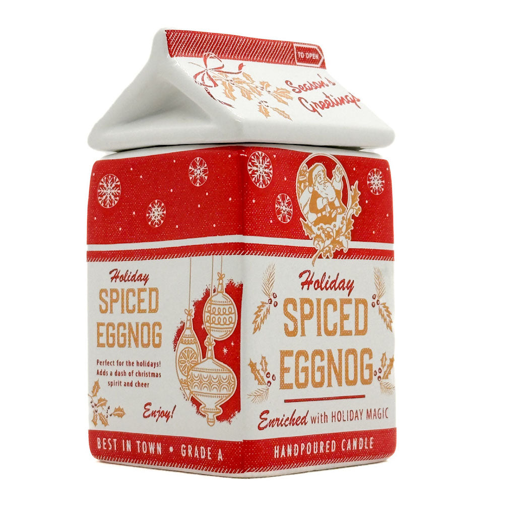 A handpoured candle in a house-shaped tin with a red and white holiday design, featuring illustrations of ornaments, snowflakes, and the text 'Holiday Spiced Eggnog'.