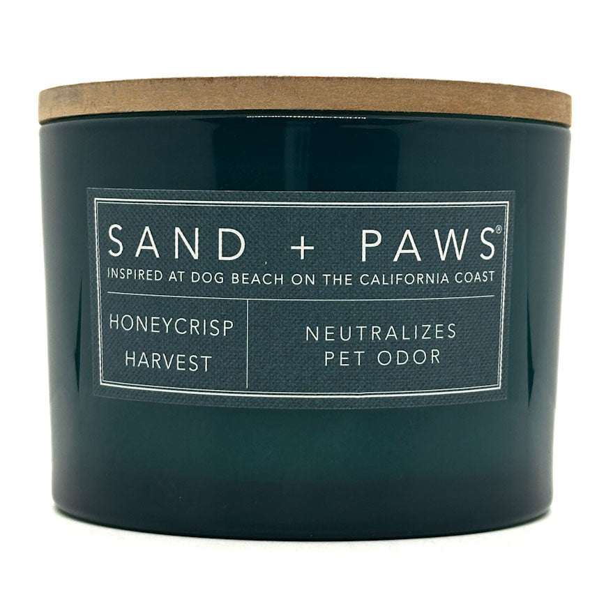 Honeycrisp green candle labeled 'Sand + Paws' with a wooden lid on a white background