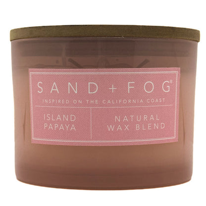 A Sand + Fog candle in a translucent amber-brown glass jar with a muted olive lid and a pink label reading 'ISLAND PAPAYA' and 'NATURAL WAX BLEND'.