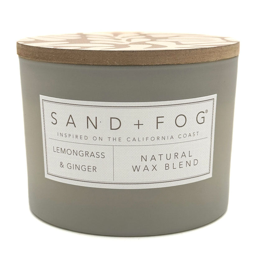 Gray Lemongrass & Ginger candle with a wooden lid labeled 'Sand + Fog' on a white background