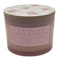 Linen & Lillies scented candle with floral lid and 'Sand + Fog' label on a white background