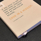 Notebook with a quote by Elizabeth Gilbert on a dark textured surface