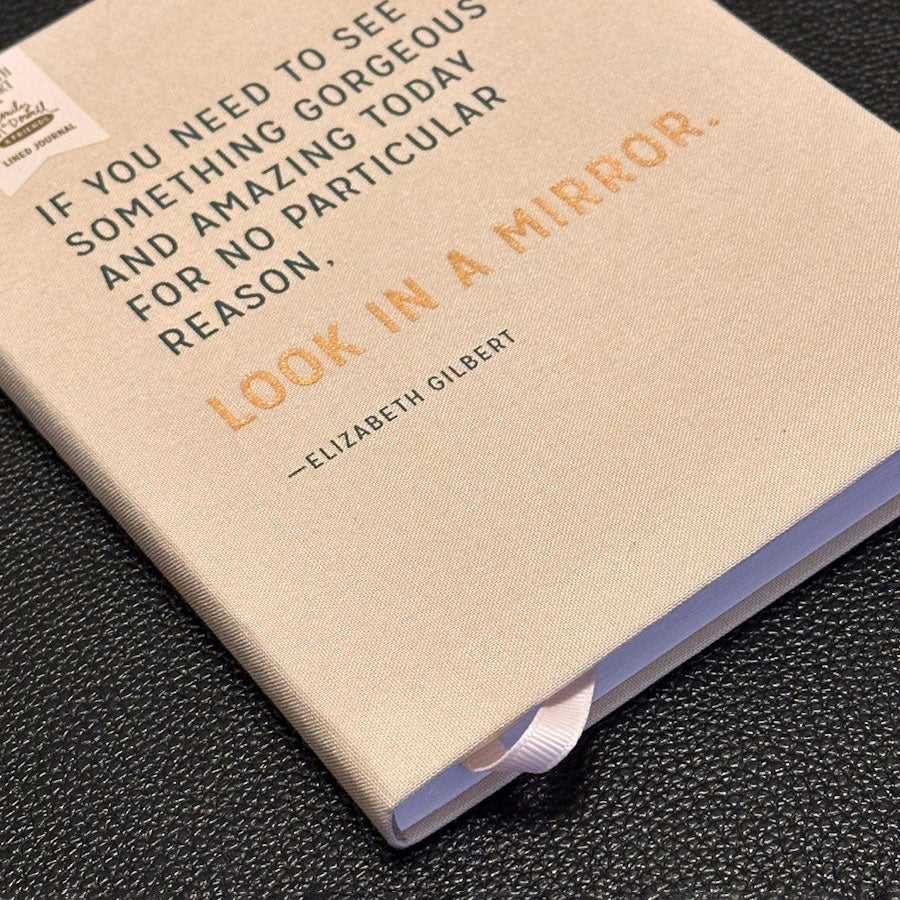 Notebook with a quote by Elizabeth Gilbert on a dark textured surface