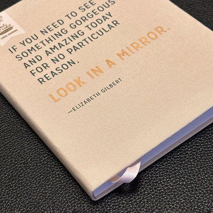 Notebook with a quote by Elizabeth Gilbert on a dark textured surface