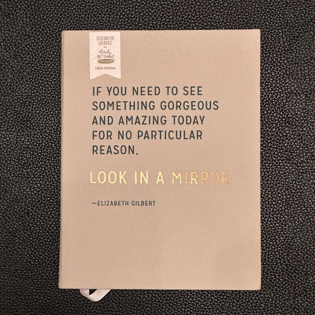 Notebook with a quote by Elizabeth Gilbert on a textured black background