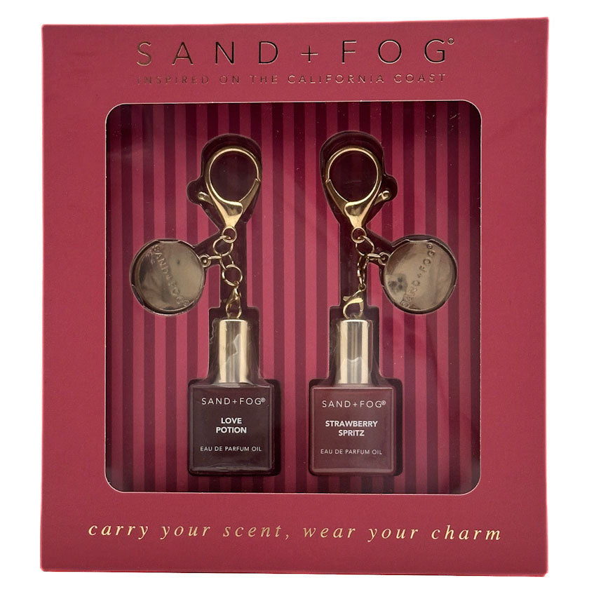 Sand + Fog perfume oil gift set in a burgundy box, containing Love Potion Perfume Oil and Strawberry Spritz Perfume  Oil, each with a gold keychain and round medallion.