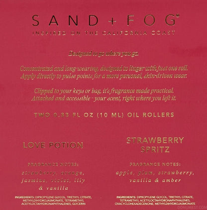 A close-up of a Sand + Fog fragrance oil card showing the 'Love Potion' and 'Strawberry Spritz' scents on a deep red background with gold text.