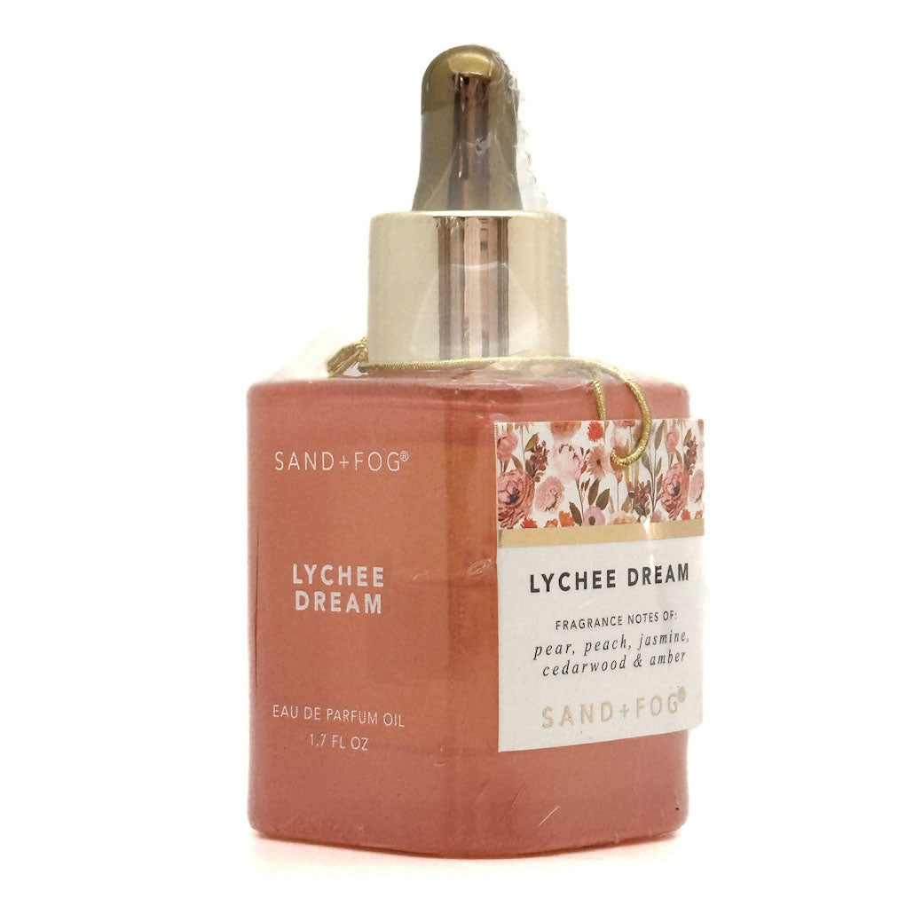 A bottle of Sand + Fog Lychee Dream Eau de Parfum Oil, featuring a terracotta-colored bottle with a metallic gold dropper cap and a floral label.