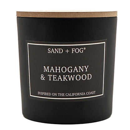 A black jar candle with a light wood lid and a black label reading 'SAND + FOG' and 'MAHOGANY & TEAKWOOD' on a white background.