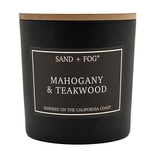 A black jar candle with a light wood lid and a black label reading 'SAND + FOG' and 'MAHOGANY & TEAKWOOD' on a white background.