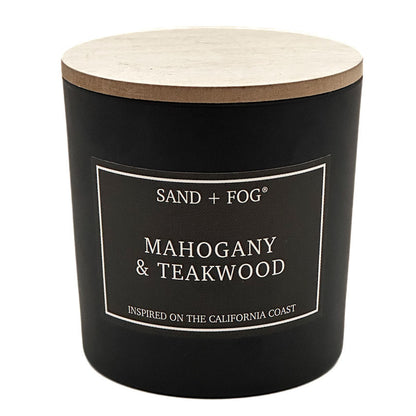 A black jar candle with a light wood lid and a black label reading 'SAND + FOG' and 'MAHOGANY & TEAKWOOD' on a white background.