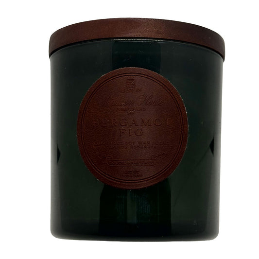 A dark green glass jar candle with a brown lid and a brown circular embossed label reading Bergamot Fig by Whittell & Hall.