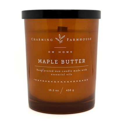 An amber glass jar candle with a black lid and white printed label text reading 'Charming Farmhouse DW HOME Maple Butter' on a plain white background.