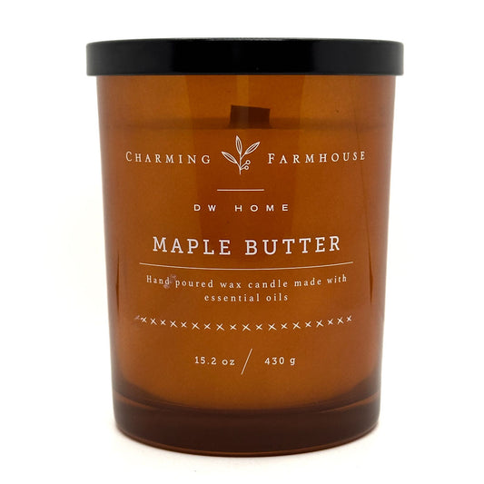 An amber glass jar candle with a black lid and white printed label text reading 'Charming Farmhouse DW HOME Maple Butter' on a plain white background.