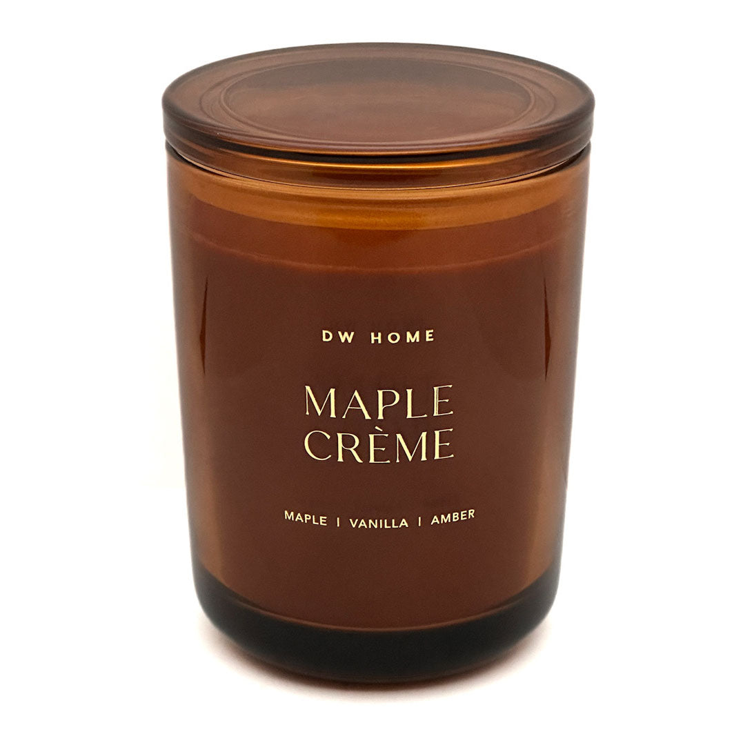 An amber glass jar candle with a matching amber lid, featuring gold lettering that reads 'DW HOME MAPLE CRÈME' on a clean white background.