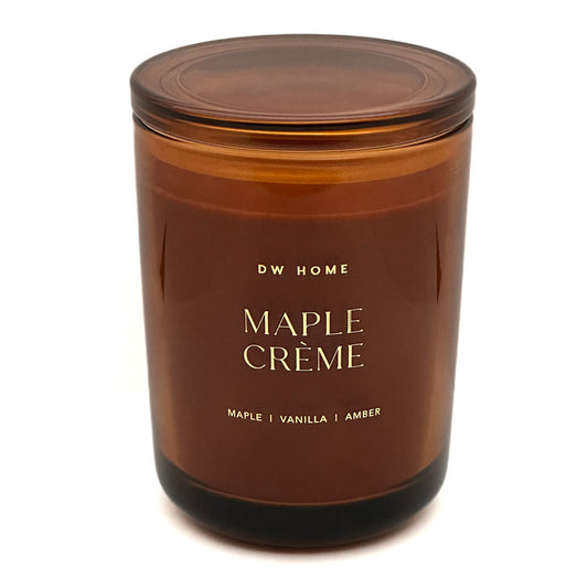 An amber glass jar candle with a matching amber lid, featuring gold lettering that reads 'DW HOME MAPLE CRÈME' on a clean white background.