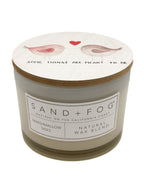 Marshmallow Skies Candle with decorative lid featuring birds and text, branded 'Sand + Fog'.
